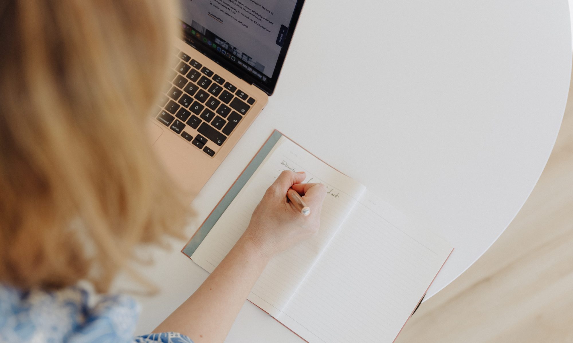Eine Frau arbeitet am Laptop und schreibt etwas auf.